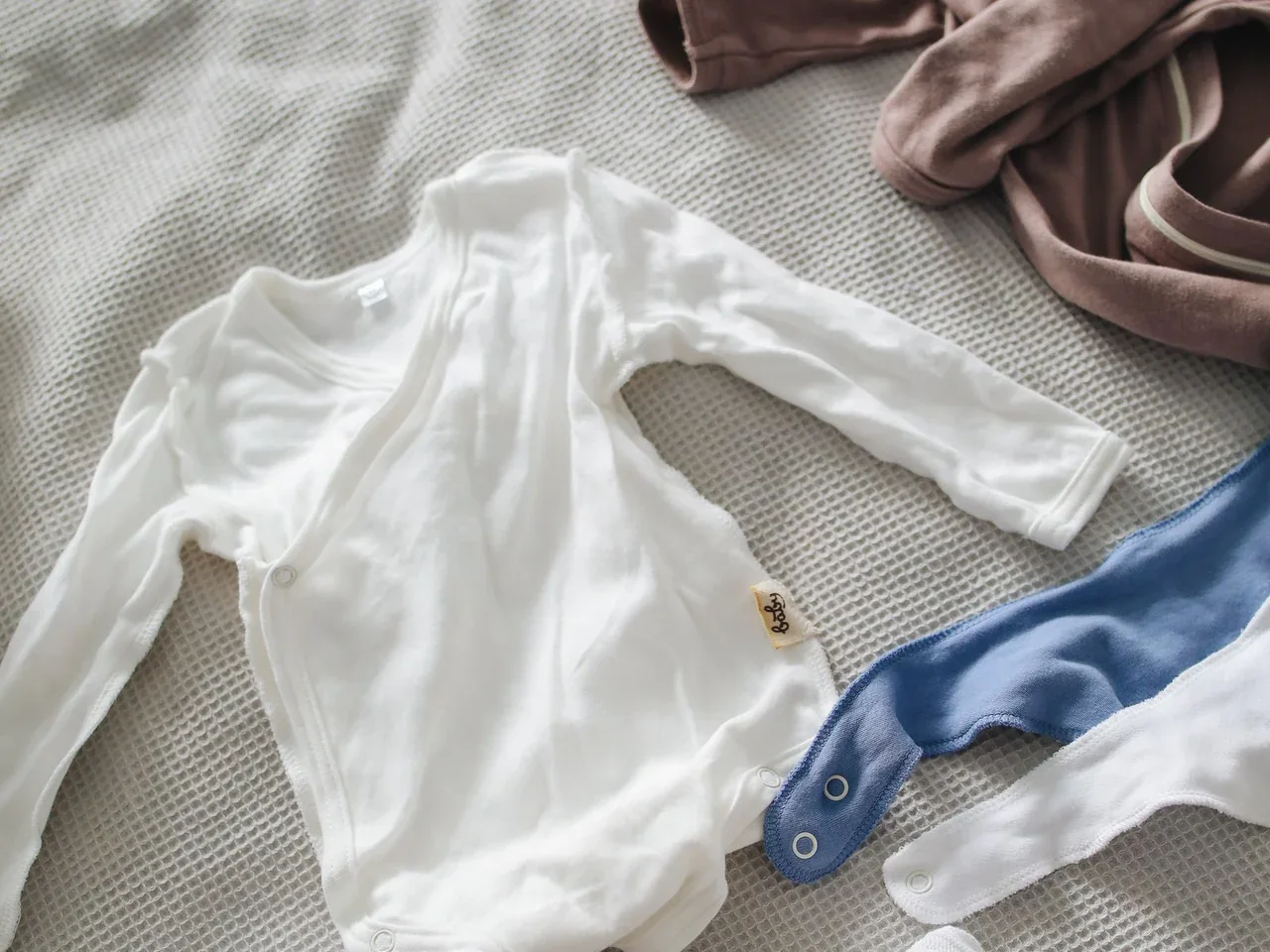 Roupas de bebê organizadas sobre tecido. Imagem ilustrativa; não representa produtos da rede.