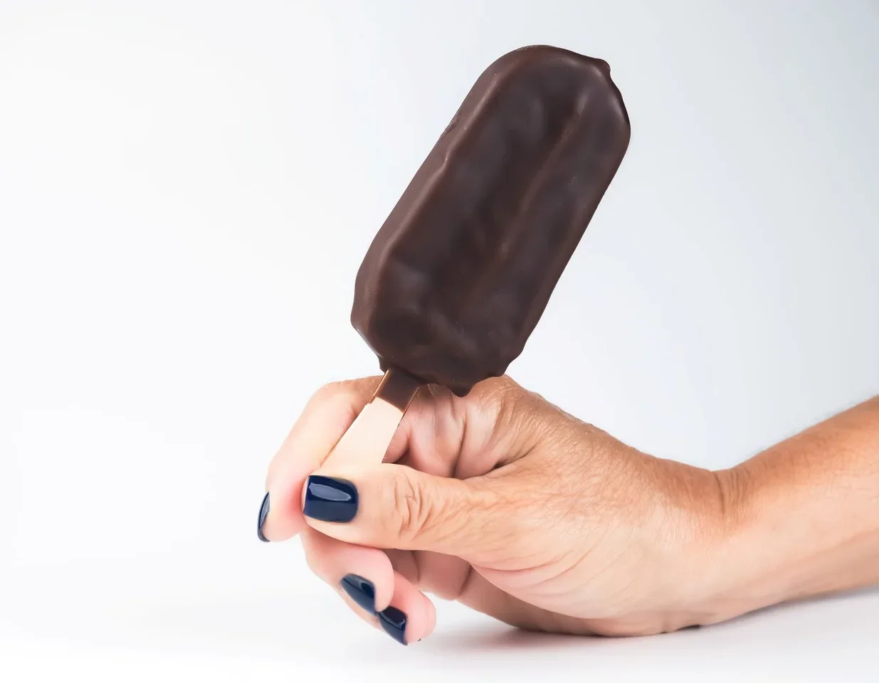 Picolé com cobertura de chocolate segurado pela mão. Imagem ilustrativa; não representa unidade, equipe ou produto da marca.