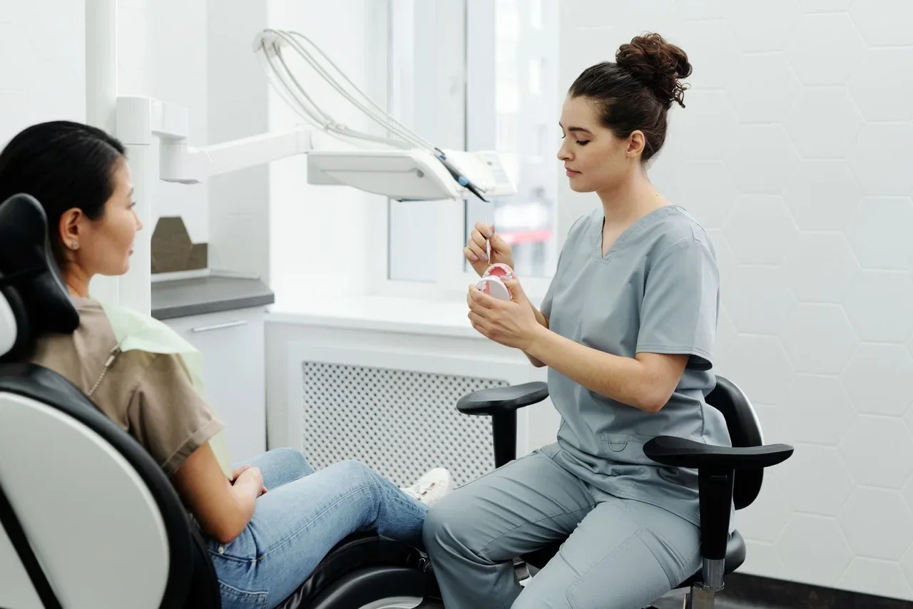 Profissional explicando um modelo odontológico a uma paciente. Imagem ilustrativa; não representa unidade, equipe ou produto da marca.